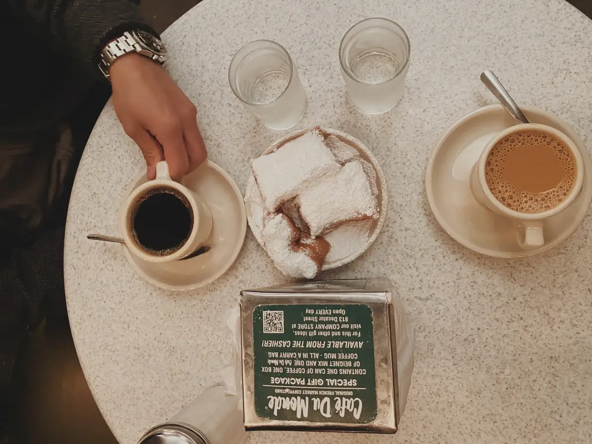 overhead view of two coffee cups and beignets on a cafe table in Cafe du Monde Cafe in New Orleans French Quarter