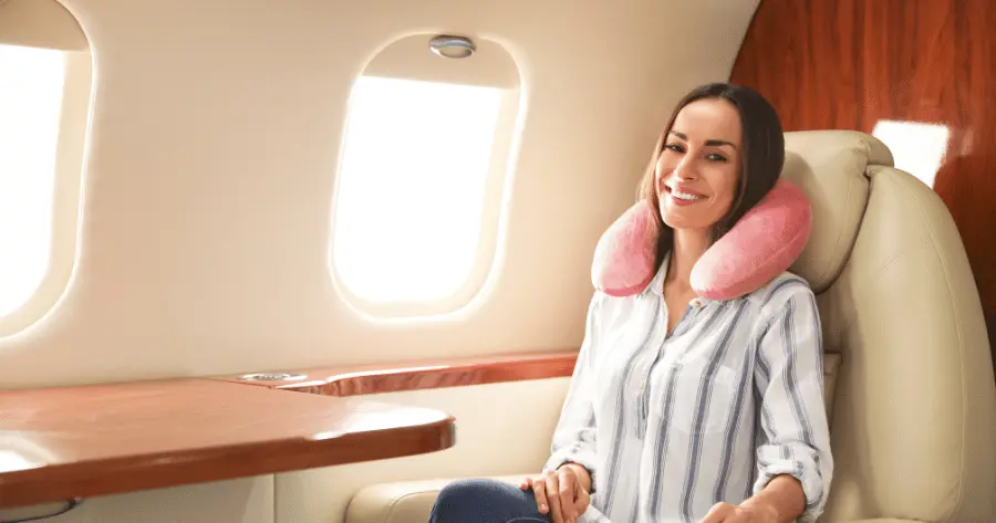 A woman waits for airplane takeoff, wearing a neck pillow for comfort.