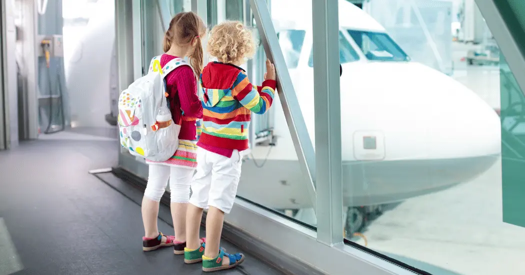 Two colorfully dressed children at an airport looking at planes through a window.