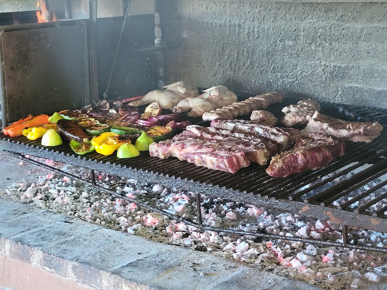 Traditional Argentinian asado, outdoor wood grill grilling beef steaks, sausages, chicken halves, and vegetables.