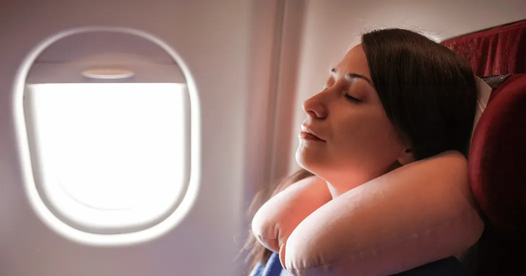 A woman leans back to sleep using a travel pillow for comfort on an economy flight.