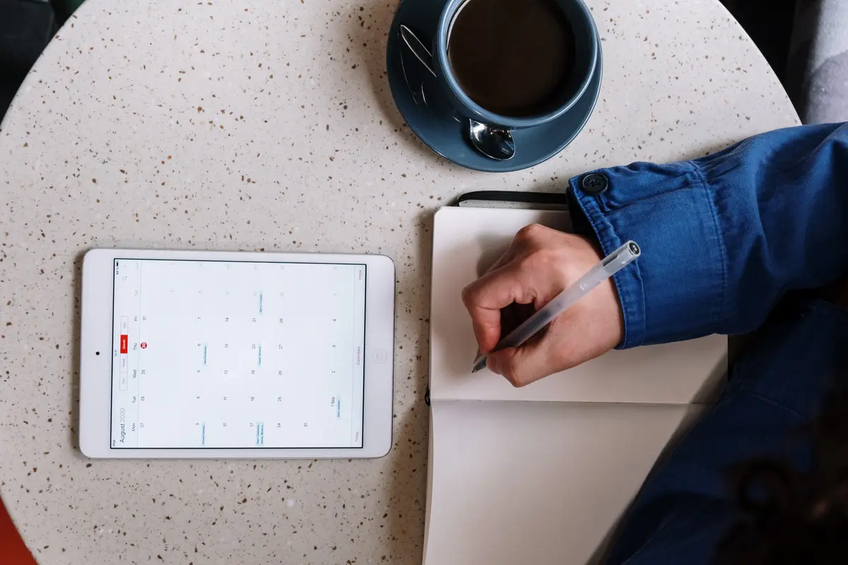 open notebook, calendar on a tablet, and a coffee cup