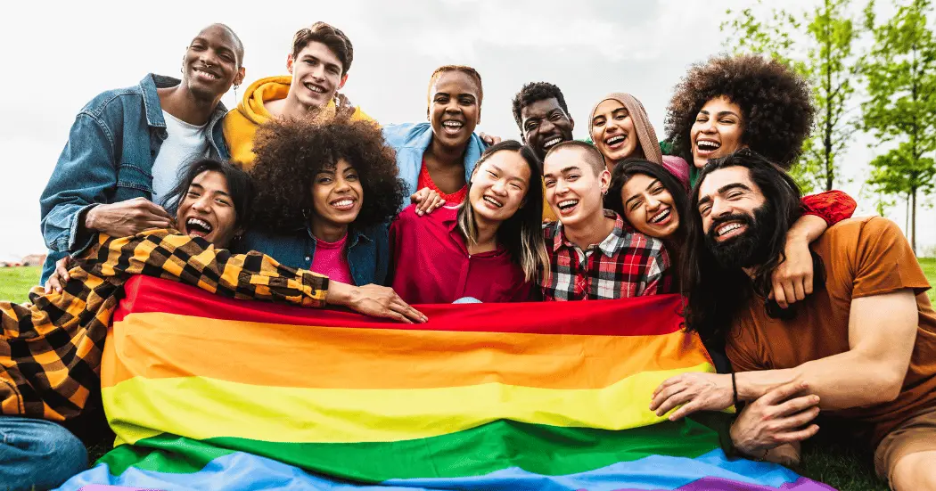 At a Pride event celebration, a group of people smiling pose with a pride flag.