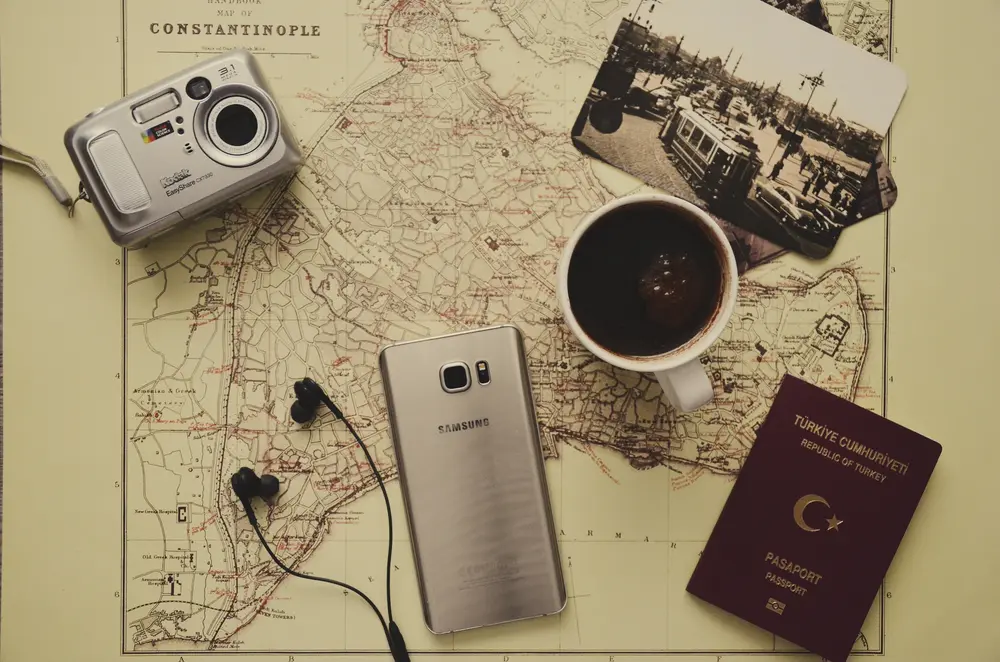 6 items on an old map of Constantinople: camera, mobile phone, headphones, passport, photograph, and coffee cup.