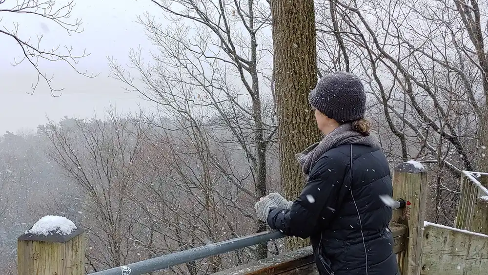 A woman in parka, gloves, and hat on a hilltop lookout in the snow in western Michigan.