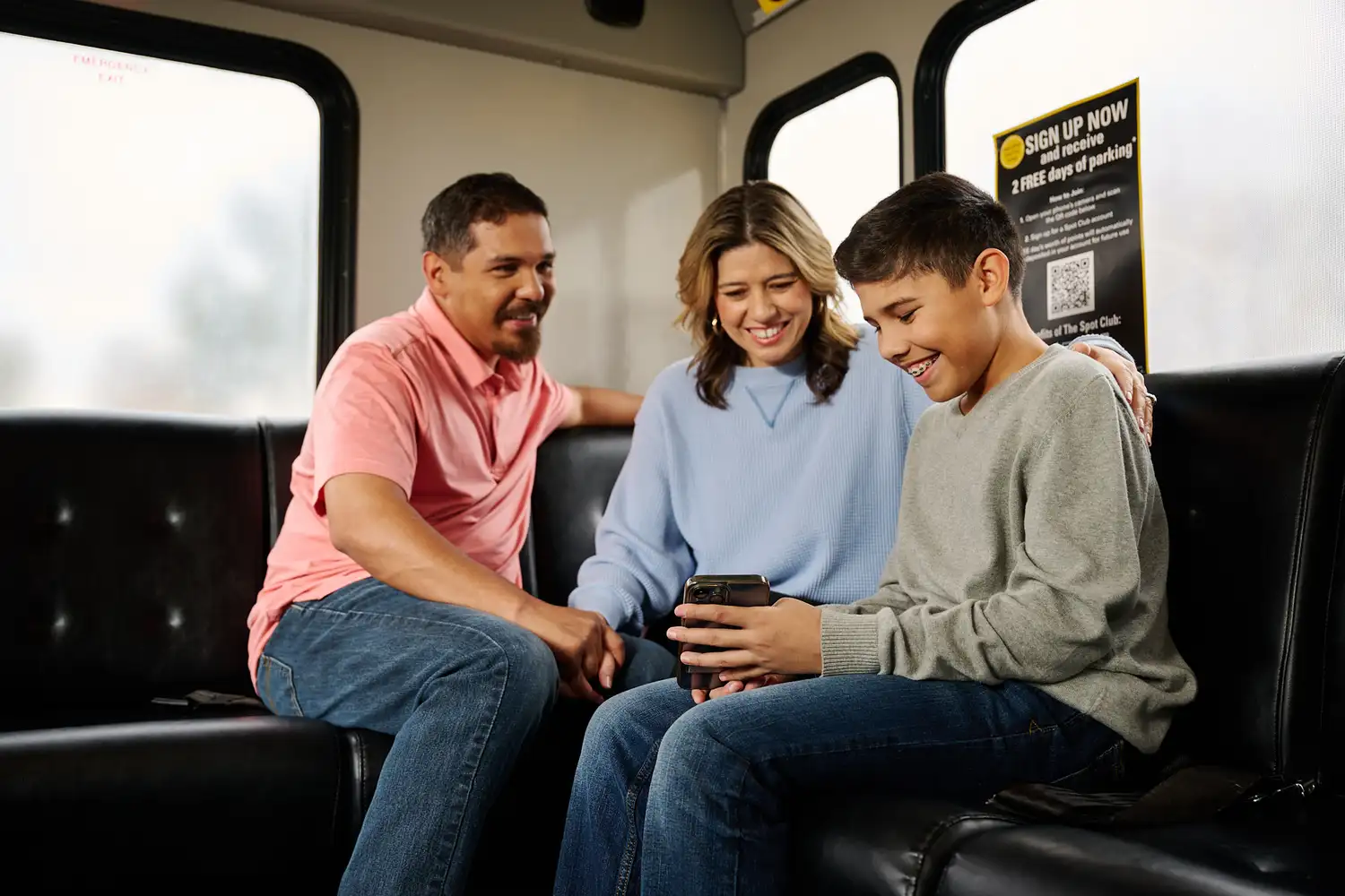 A family of three inside an Airport Shuttle checks in on a mobile device.