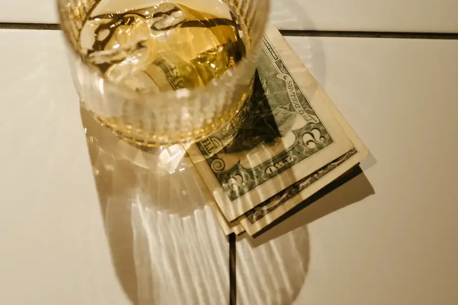 A cash tip under a cocktail glass on a tile table top.