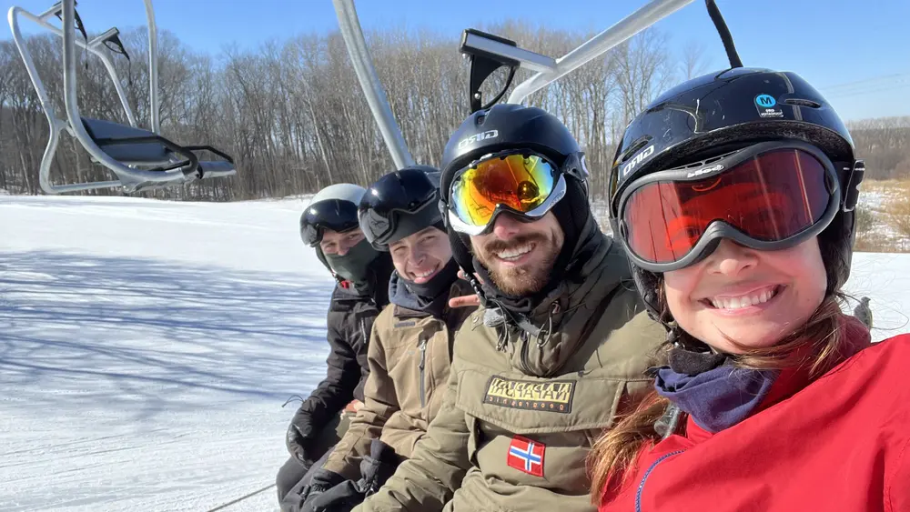 A family of four on a ski lift wearing ski goggles.