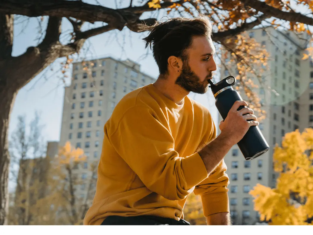 A man drinks from his water bottle while sitting out in the autumn breeze